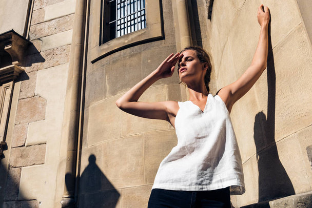 Woman in a white T-shirt standing on the street, shading her face from the sun with shadows. - Foto, imagen
