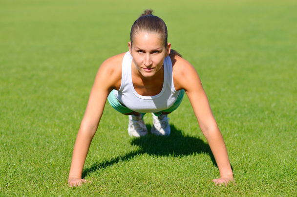 Attractive young woman doing stretching exercises on grass before run - 写真・画像