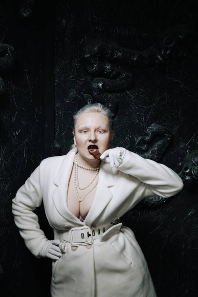 Nuori friikki plus koko albiino nainen ahneesti syö ja rakastaa suklaata mustalla pohjalla. kurvikas lyhyet hiukset tyttö valkoinen asu
. - Valokuva, kuva