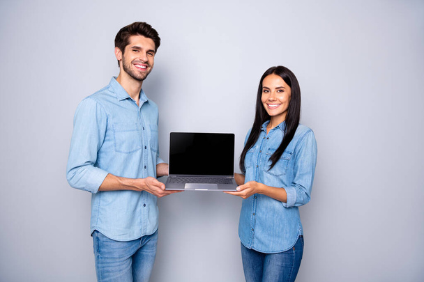 Photo of cheerful charming couple fun positive of two people presenting laptop advertising holding hands wearing jeans denim shirt isolated over grey color background - Fotografie, Obrázek