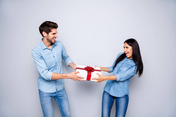 Photo of cheerful trendy stylish white couple of two people together contesting about who will obtain the giftbox wearing jeans denim isolated over grey color background - Foto, afbeelding