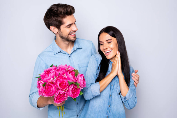 Photo of beautiful nice cute couple of two people girlfriend rejoicing with receiving bouquet of fuchsia flowers and boyfriend hugging her from back in jeans denim isolated grey color background - Photo, Image