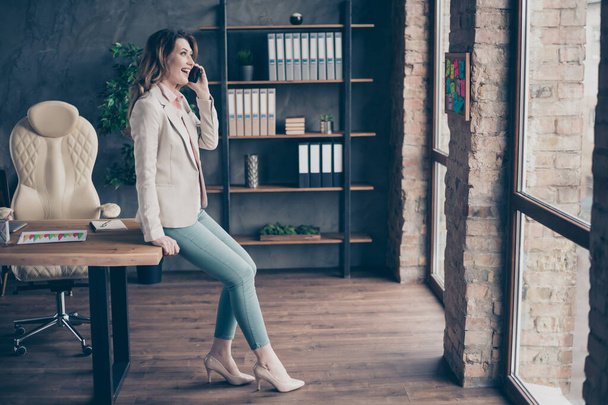 Profile side full length body size view of nice-looking attractive charming stylish trendy cheerful mature lady shark director talking on phone at industrial style interior work place station - Foto, afbeelding