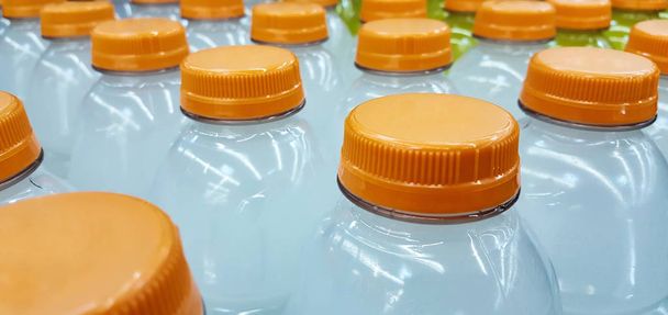 Rzędy generycznych napojów butelkowanych z pomarańczowymi wieczkami pod kątem ukośnym. Większość zawiera biały płyn, ale najdalsze zawierają żółty.  - Zdjęcie, obraz