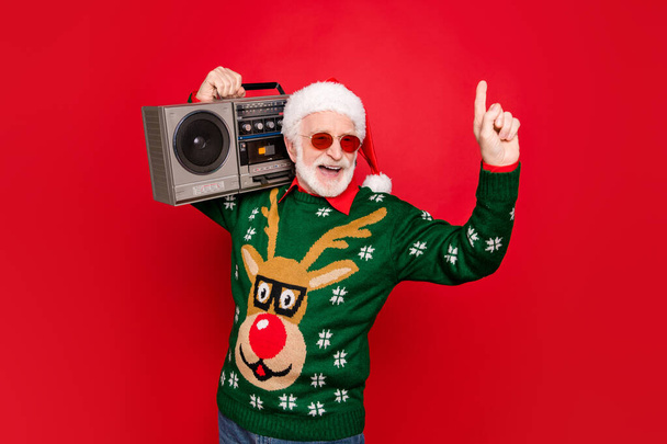 Photo of elderly funny santa man hold vintage tape recorder chilling at youngster party long waited guest wear specs x-mas ugly ornament sweater cap isolated red background - Foto, imagen