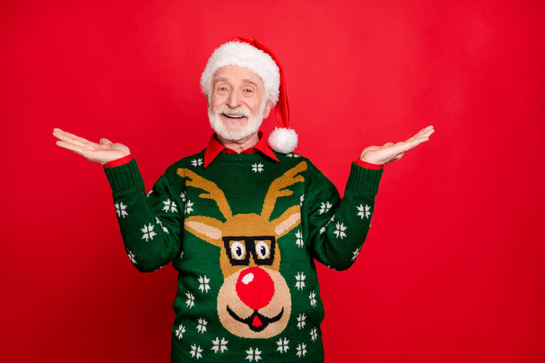 Photo of santa senior man holding sale products on open palms advising low holiday prices wear x-mas ugly ornament sweater isolated red background - Fotó, kép