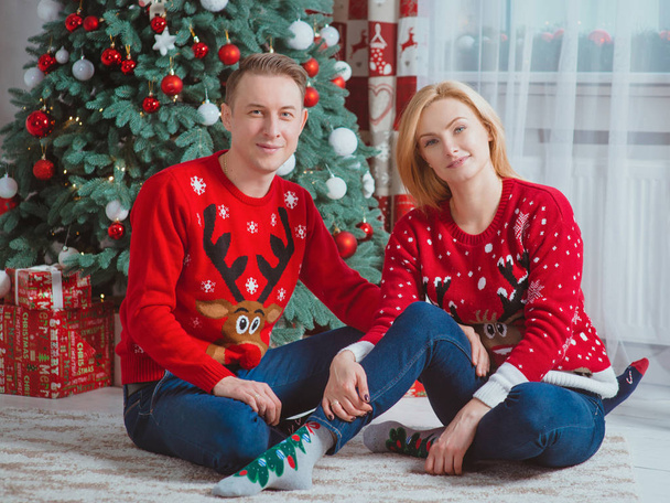 krásný, šťastný kavkazský pár (rodina) v džínách a vánočních svetrech u vánočního stromku doma. Koncept Vánoc a Nového roku - Fotografie, Obrázek