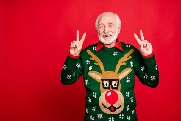 Portrait of positive cheerful grey hair old man enjoy theme noel x-mas time party make v-signs wear reindeer pattern design tradition clothes isolated over red color background - Fotó, kép
