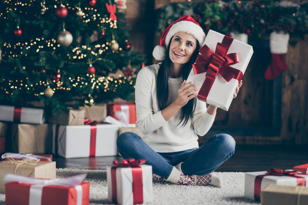 What ise here. Full length photo of cheerful jolly girl shake gift box received on christmas night enjoy x-mas newyear celebration wear santa claus headwear in house with noel ornaments indoors - Foto, imagen