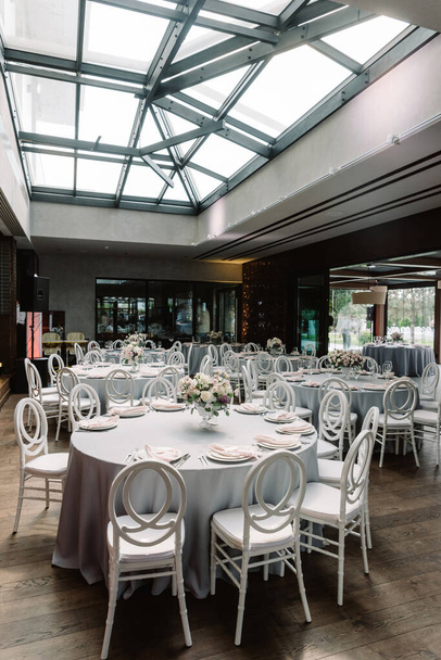 Ronde vakantie tafels in de grote ruime hal van het restaurant met glazen plafonds. - Foto, afbeelding