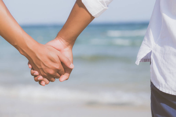 Primer plano asiático gay pareja cogida de la mano juntos en la playa ingenio
 - Foto, imagen