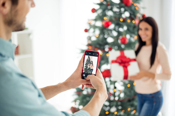 Back side blurred photo of two people man making photo on his cell phone of wife hold package gift for christmas time x-mas holidays in house indoors - Φωτογραφία, εικόνα