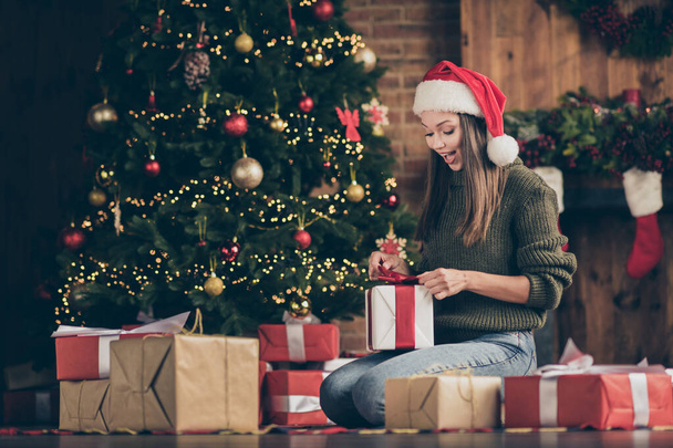Wow its for me. Full length photo of excited emotional girl sit floor checkered plaid blanket get gift box for christmas enjoy newyear noel present wear santa claus headwear in house indoors - 写真・画像