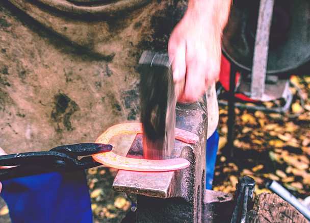 Ferreiro segura ferradura em alicates e deita-a fora com martelo
 - Foto, Imagem