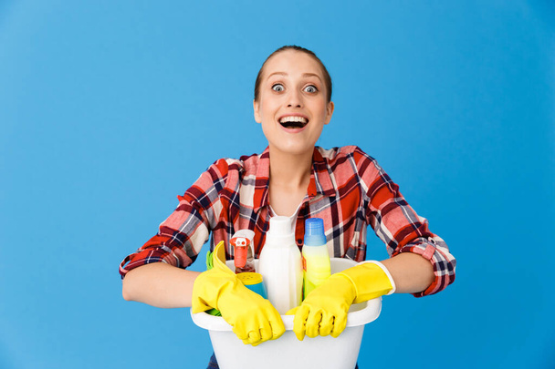 Portrait of joyful housewife in rubber gloves holding basin with - 写真・画像