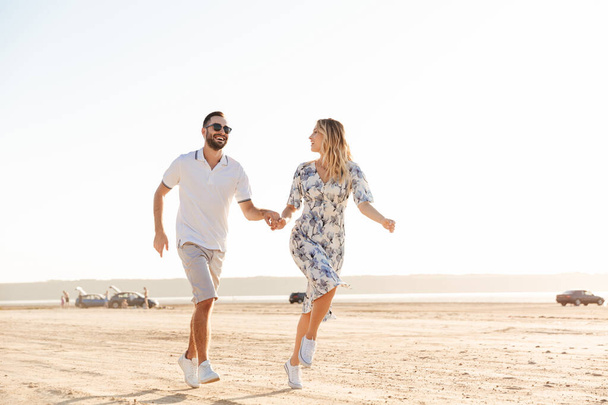 Photo of caucasian happy couple smiling and running on sunny beach - Φωτογραφία, εικόνα