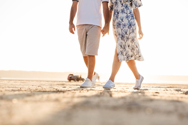 Cropped photo of beautiful caucasian couple holding hands together while walking on sunny beach - Фото, изображение