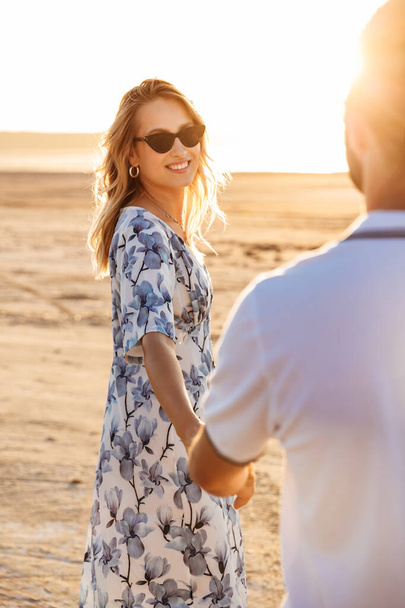 Photo of happy beautiful couple smiling and holding hands together while walking on sunny beach - Foto, Bild