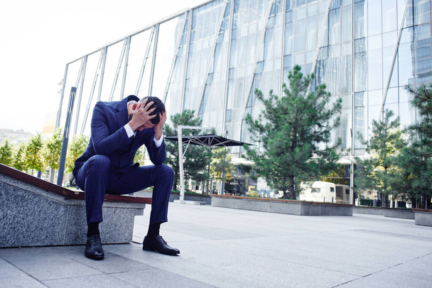 Financial ruined desperate businessman at the entrance to a glass office building, concept of bankruptcy - Фото, изображение