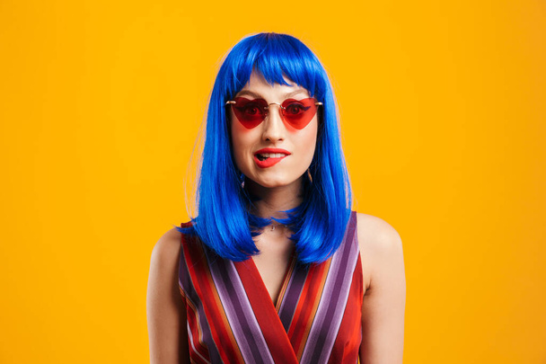 Portrait closeup of seductive woman wearing blue wig and sunglasses looking at camera and biting her lip - Fotó, kép