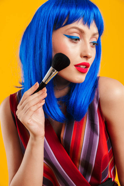 Portrait of seductive alluring woman wearing blue wig looking aside and applying powder with brush - Foto, imagen