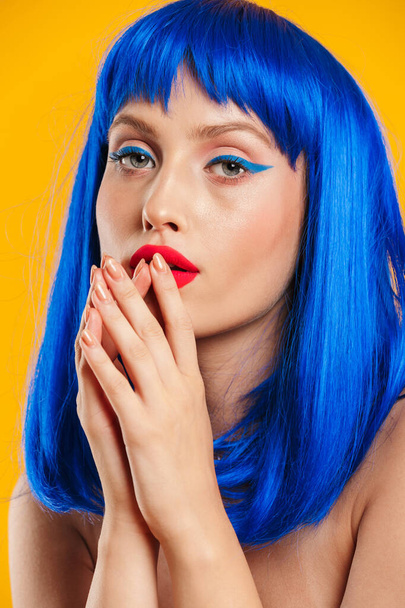 Portré közelkép a szexuális nő visel kék paróka néz kamera és kézen fogva a szája mellett - Fotó, kép