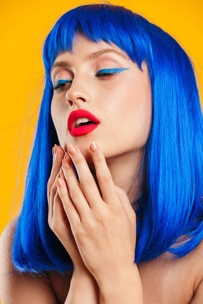 Πορτρέτο closeup της σεξουαλικής γυναίκας φορώντας μπλε περούκα κοιτάζοντας προς τα κάτω και κρατώντας τα χέρια κοντά στο στόμα της - Φωτογραφία, εικόνα
