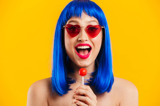 Portrait of glamorous astonished woman wearing blue wig and sunglasses holding lollipop - Fotó, kép
