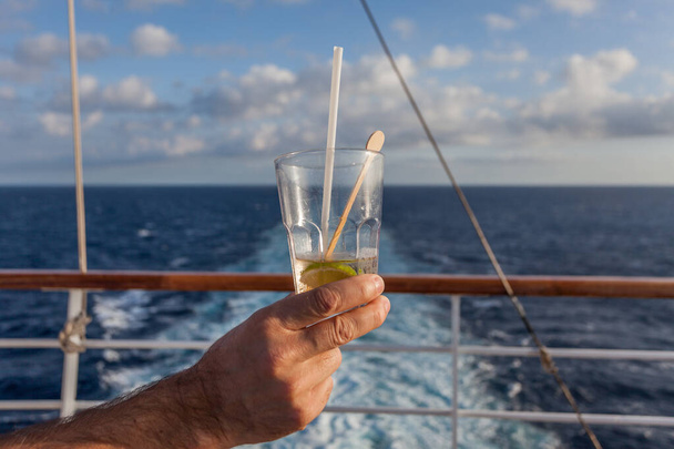Ręka osoby trzymającej szklankę ginu z tonikiem, z morzem w tle - Zdjęcie, obraz