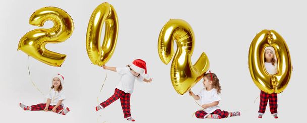 Kids party, people and new year holidays concept - little children girls in Santa hats celebrating new years eve 2020. Golden air balloons numbers shape isolated on white background. Christmas holiday - Photo, Image