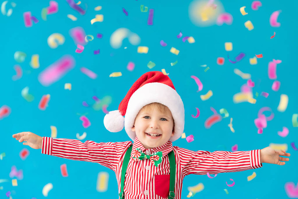 Happy child dressed Santa Claus hat against blue background - Foto, afbeelding