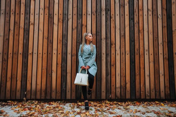 Una chica con un abrigo de otoño y una bolsa en el backgrou de madera
 - Foto, Imagen