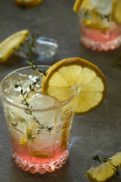 Bebida fresca con limón y tomillo en un vaso sobre un fondo gris
 - Foto, Imagen