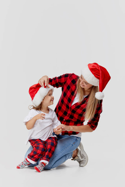 Christmas time. Happy hugging family, mother and daughter, little child playing in Santa hats, isolated on white. New year holiday concept - Foto, Bild