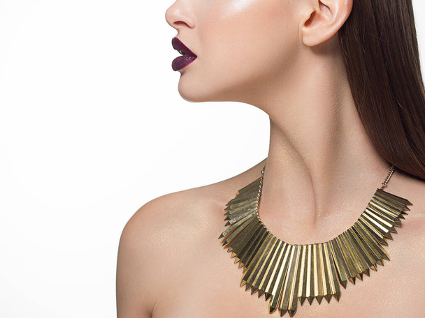 Close up glamorous image of a female predator with a bite of purple lips. On the neck are golden jewels and sparkles on the body. Beautiful transparent skin. Spa care or beauty care. Beauty sexy woman - Foto, Imagem