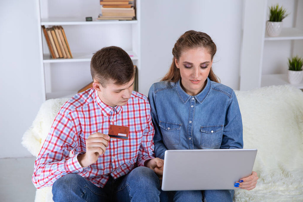 Casal fazendo compras on-line sentado em casa no sofá e usando cartão de crédito
. - Foto, Imagem