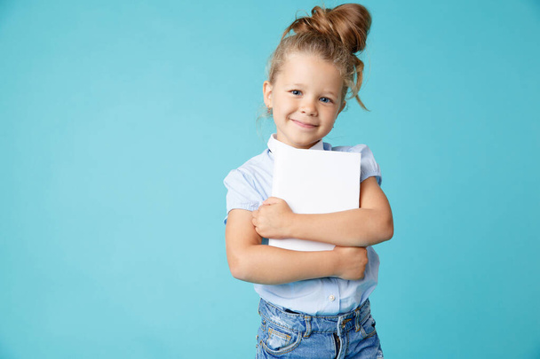 Милая маленькая счастливая девочка, стоящая с книгой на синем фоне
. - Фото, изображение