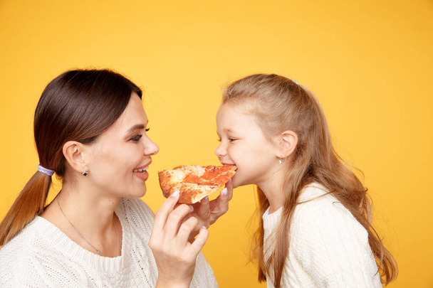 母と娘食べるピザ一緒にと楽しみを持っていますオフザ黄色のスタジオ. - 写真・画像