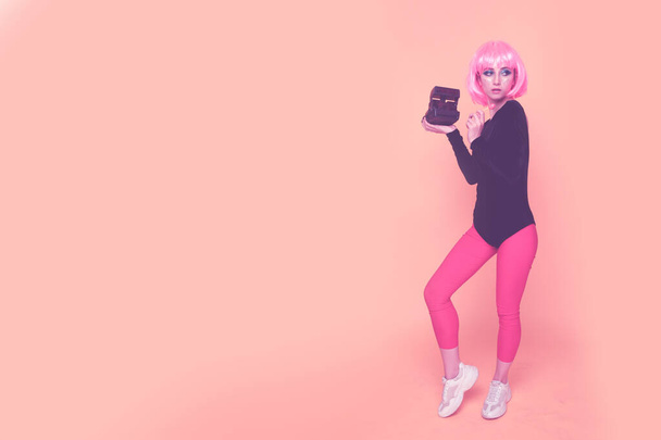 Concepto de moda de los 90. Chica en una peluca rosa sosteniendo la cámara
. - Foto, imagen