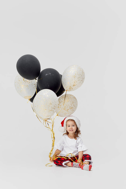 Happy child girl in Santa hat with golden silver balloons, celebrate new year and christmas holidays. New year eve celebration. Party decor and design for birthday and anniversary on white background - Fotoğraf, Görsel