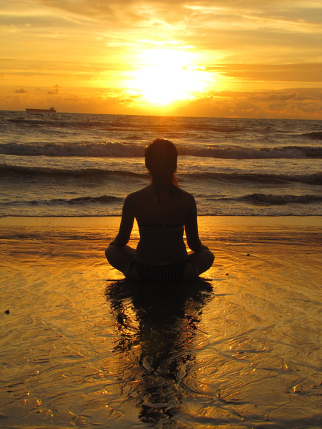 junge Frau am Strand sitzend, Silhouette bei Sonnenuntergang. junge Frau praktiziert Yoga im Freien. Harmonie und Meditationskonzept. Gesunder Lebensstil. Meditieren im Lotus Yoga - Foto, Bild