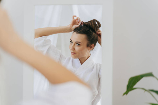 Smiling young woman is doing hairstyle at home - Φωτογραφία, εικόνα