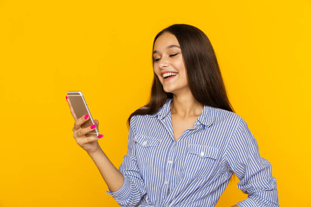 щаслива жінка з мобільним стоянням і посмішкою ізольована на жовтому тлі
. - Фото, зображення