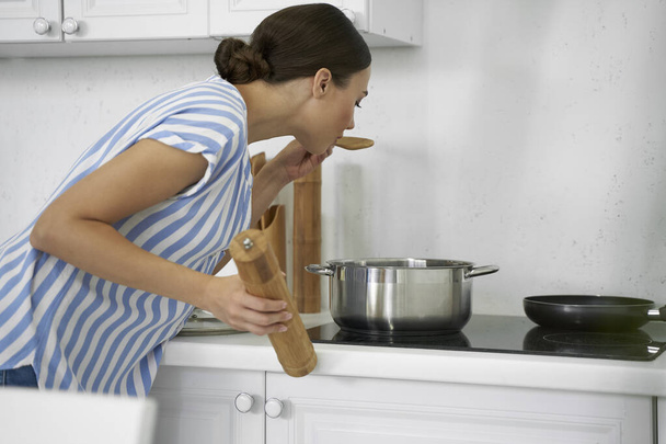 Young woman tasting meal while cooking stock photo - Foto, Imagem