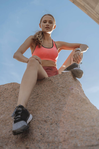 Young sportive lady is sitting on rock ledge - 写真・画像