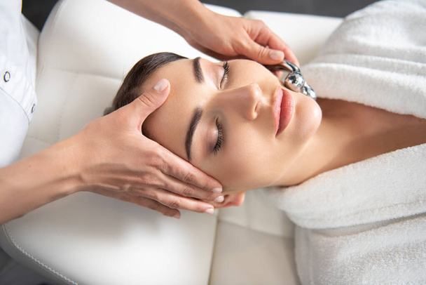 Beautiful young woman receiving face lifting massage at beauty salon - Foto, imagen