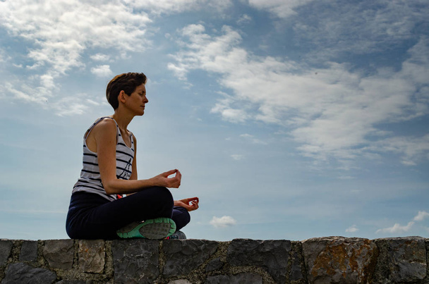 Mujer sentada en una pared, haciendo yoga
. - Foto, imagen