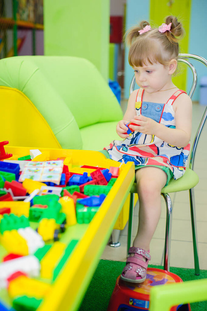 Cute little girl enjoying while playing with toys or blocks, sitting at table. child girl playing wooden toys at home or kindergarten - Foto, imagen