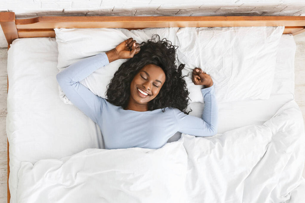 Top kilátás mosolygós nő nyújtózkodik az ágyban - Fotó, kép