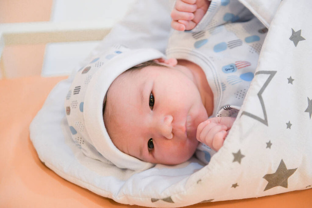 Baby im Krankenhaus, auf dem Sofa liegend, in eine Decke gehüllt, Entlassung aus der Geburtsklinik, Geburt des Kindes. schlafendes süßes Neugeborenes, in eine Babydecke gewickelt, in Acryl - Foto, Bild